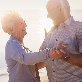 An elderly couple smiling and dancing together on a beach